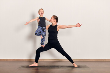 Fototapeta premium Young woman and child practice yoga together on mat. Both exhibit balance and focus, creating harmonious pose. Bright studio with wooden floor enhances serene atmosphere
