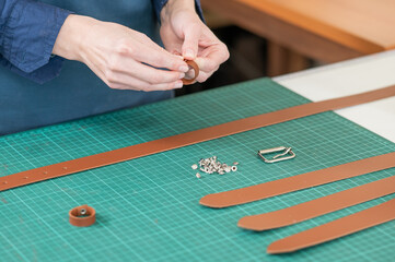 A woman attaches accessories to a leather belt. Leatherworker's workshop. 