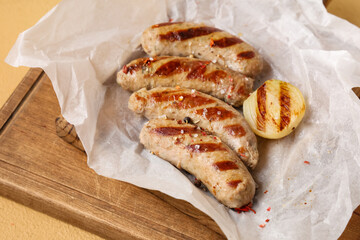 Wooden board with tasty grilled sausages on beige background