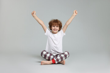 Cute little boy in pajamas on grey background