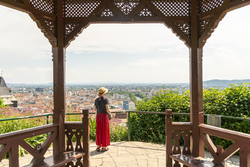 View of a woman in a red skirt standing in a wooden gazebo gazing out at the cityscape and greenery, Graz, Styria, Austria.