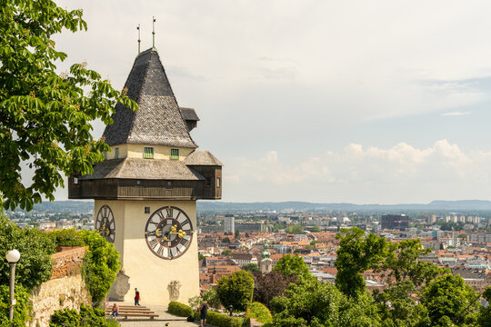 View of the iconic clock tower, its face gleaming in the sunlight, stands tall overlooking the cityscape with lush greenery, Graz, Styria, Austria.