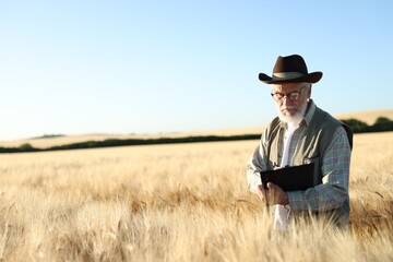 Senior farmer with clipboard in field of ripe wheat outdoors, space for text