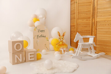 Minimalist first birthday party arrangement featuring pastel balloons, a bunny in a yellow dress, a...