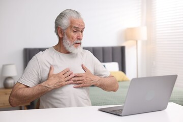 Senior man having online consultation with doctor via laptop at table indoors