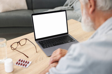 Senior man having online consultation with doctor via laptop at table indoors, closeup