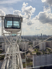 Close up shot of modern Ferris wheel cabin against the backdrop of scenic city view. The image captures the structure's detailed design with a clear blue sky and residential buildings below