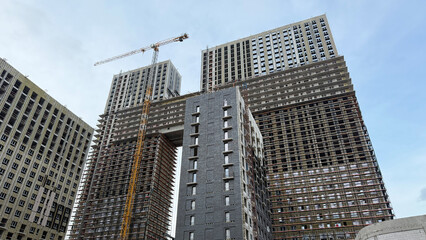 Fototapeta premium Construction site of two tall residential buildings under development, with scaffolding and crane, showcasing the modern building process and urban architecture in progress