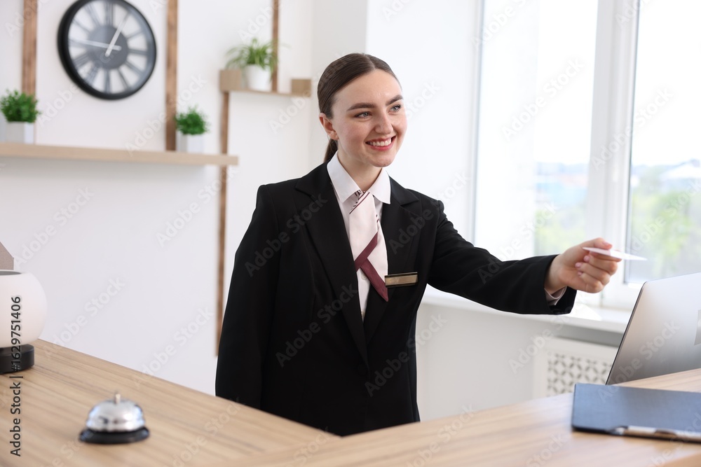 Poster smiling receptionist in uniform giving card key at reception desk in hotel
