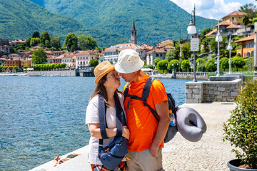Tourist couple enjoys leisurely walk along Mergozzo Lake, Italian lakeside town, village, taking photos, enjoying scenic mountain view, bonding and relaxing