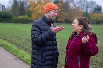 Older mother and adult son argue in autumn park, emotional distance, family conflict, generational...