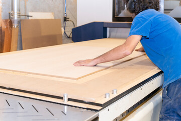 Carpenter carefully positioning wood panel on modern cnc router in professional workshop, preparing for precise cutting and woodworking