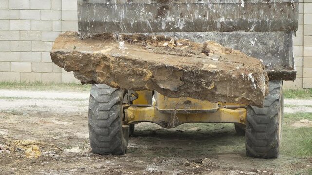 Excavator heavy machinery lifts large dirt rock slab construction site