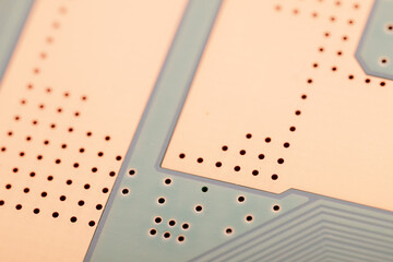 Close-up photo showing a printed circuit board with exposed copper pads, drill holes, and precise trace patterns for electronics.