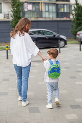Mother walking son to school with backpack.