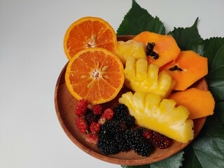 Fresh oranges, pineapple, blackberries and papaya on the wooden plate isolated on white background. Mix fresh fruit in summer