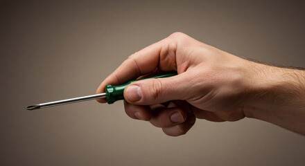 A male hand holding a green handled crosshead screwdriver, ready for repair or construction work on a neutral background.