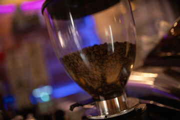 Coffee beans stored in glass hopper of professional grinder in cafe