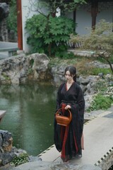 Young Asian female in traditional clothing by a tranquil pond.