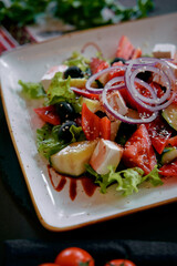 A Colorful and Fresh Salad Featuring Sliced Tomatoes, Cucumbers, Black Olives, Onions, Feta Cheese, and a Drizzle of Balsamic Vinegar on a White Plate