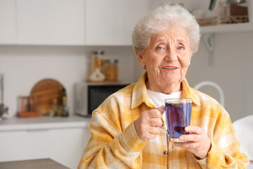 Senior woman with glass cup of butterfly pea flower tea in kitchen