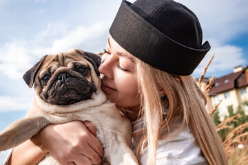 Young happy beautiful woman holding, kissing and hugging her beloved dog during a walk with harness...