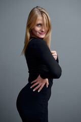 Confident Woman in Black Dress Striking a Stylish Pose against Gray Background