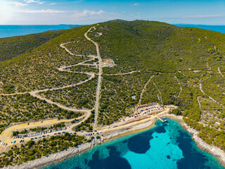 Aerial view of a winding unpaved road on Cres Island descending from a forested hilltop to a rocky...