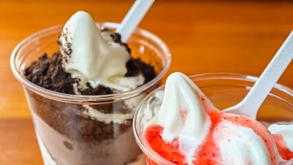 Close-up of two ice cream sundaes in clear plastic cups, ready to eat.