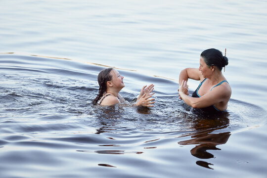 Mother and daughter interact and enjoy recreational swimming in calm outdoor water, expressing joy and connection.