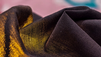 Close-up view of dark fabric with vibrant yellow-gold stains and folds.