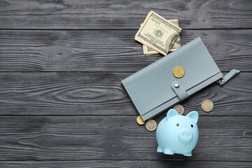 Blue piggy bank with dollar banknotes, coins and wallet on black wooden background