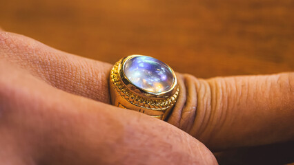Close-up of a hand wearing a gold ring with a blue, iridescent stone.