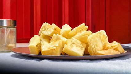 A plate of pale yellow diced fried cassava on a bright red background