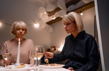 Two women share a serene moment at a dinner table, illuminated by candlelight and surrounded by festive decorations, evoking concepts of intimacy, celebration, and a cozy ambiance.