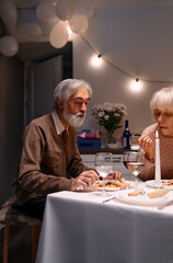 A senior couple dining together at a table with dinner settings, a lit candle, and festive decorations, enjoying a peaceful and heartfelt moment.