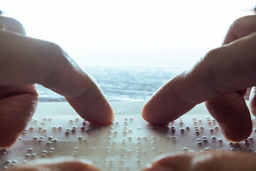 Visually impaired individuals use their fingertips to read Braille on paper, which is a tactile...