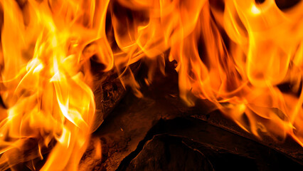 Close-up of vibrant orange and yellow flames engulfing dark wood, creating a dynamic and intense...