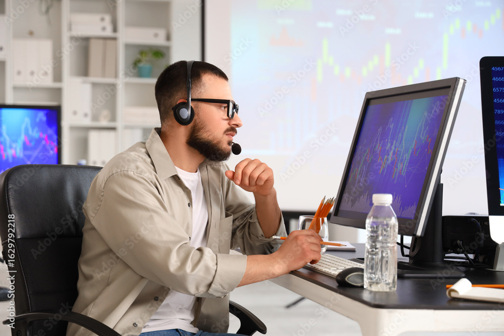 Poster male trader with headset working at table in office