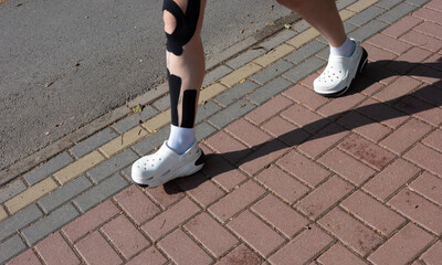 A person's legs with medical tape walking on a brick sidewalk in the sunshine.