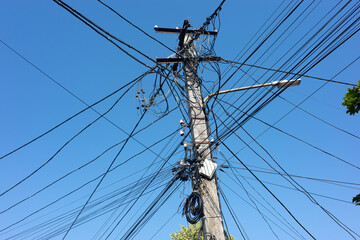 A chaotic network of wires and cables on an electricity pole, set against a bright blue sky.