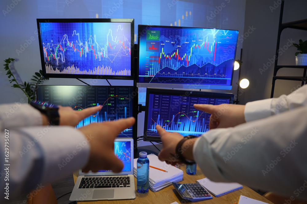 Poster hands of traders pointing at diagrams on computer monitors in dark office