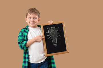 Cute boy pointing at chalkboard with drawn light bulb on beige background. Children's Inventor's Day