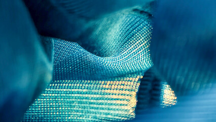 Close-up of textured blue fabric with a subtle grid pattern, showing folds and curves, creating an abstract composition.