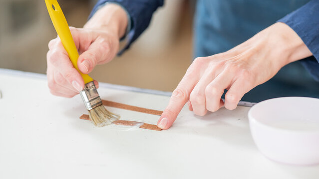 A craftsman uses a brush to cover leather parts.