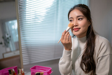 Beautiful asian woman applying makeup with brush at home in front of mirror