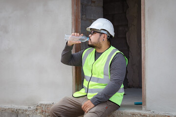 Hopeless builder worker sitting in construction site bend head down in his knee, stressed Asian...