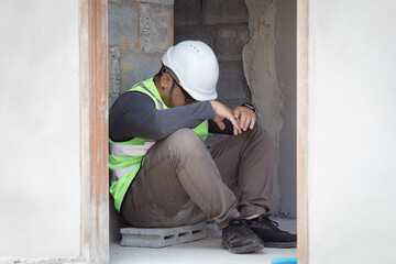 Hopeless builder worker sitting in construction site bend head down in his knee, stressed Asian...