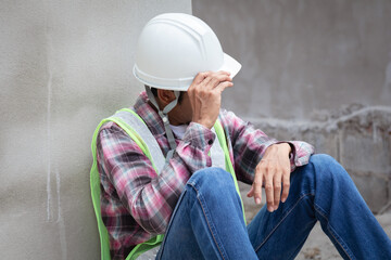 Hopeless builder worker sitting in construction site bend head down in his knee, stressed Asian...