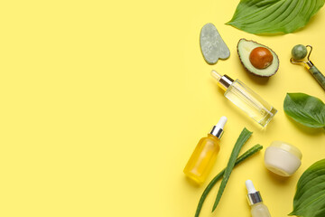 Composition with facial massage tools, bottles, jar of cosmetic products and ingredients on yellow background